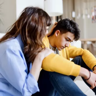 A care worker consoling a teenage boy in his room