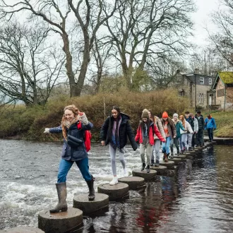 Group of adults and young people hopping across stepping stones in Devon