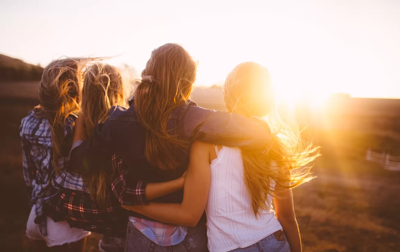 Group of teenage girls standing together in a huddle watching the sunset