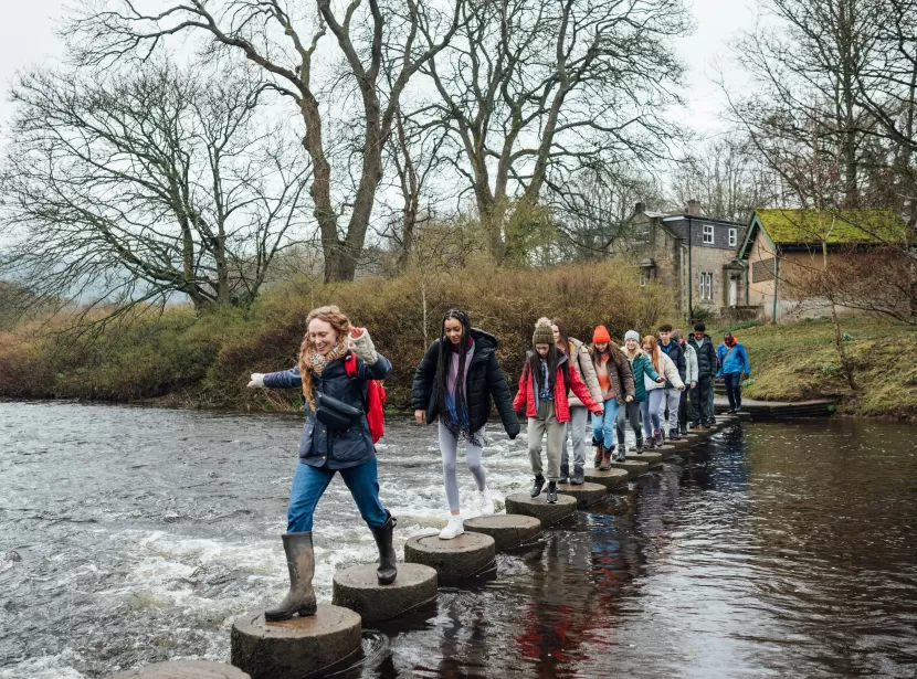 Group of adults and young people hopping across stepping stones in Devon